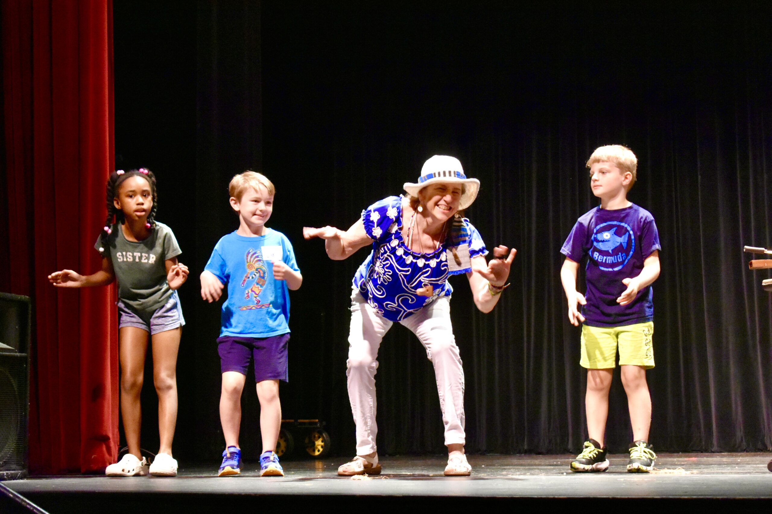 A woman on a stage with three children is telling a story.